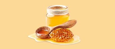 Geöffnetes Honigglas mit Holzlöffel und Bienenwabe die davor in einer Honiglache liegen