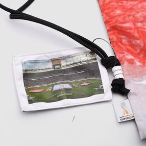Ein Stoffschild, das an einem Turnbeutel angebracht ist, ist mit einem Fußballstadion als Motiv bedruckt. 