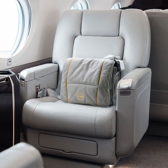 Auf einem Flugzeugsitz steht eine Tasche, die aus altem Sitzmaterial hergestellt wurde und das Lufthansalogo als Stickerei trägt.